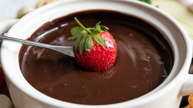 Dipping strawberry into chocolate fondue in white dish