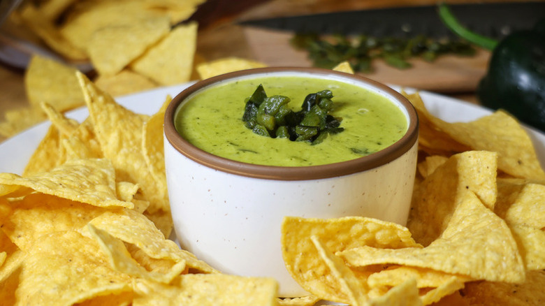 Bowl of green queso dip on plate with tortilla chips