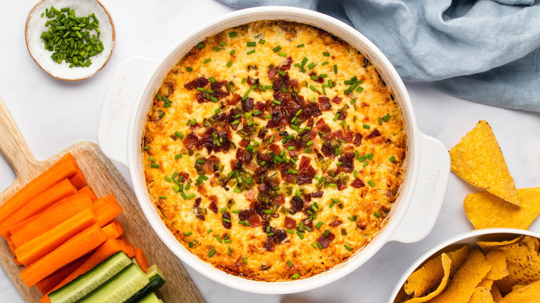 Cheesy jalapeno popper dip in baking dish next to crudites and tortilla chips