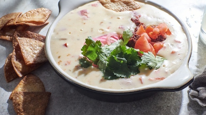 White queso dip in baking dish, topped with cilantro and diced tomatoes