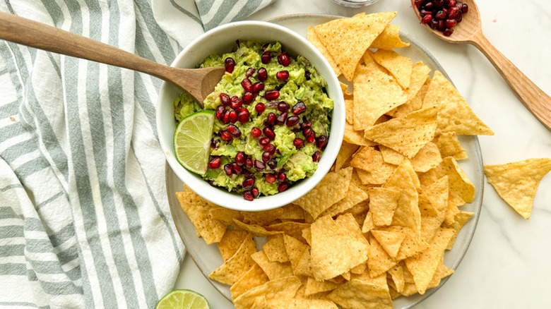 Bowl of pomegranate guacamole on plate with tortilla chips