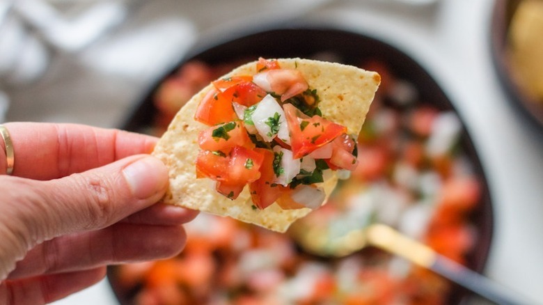 Hand holding tortilla chip topped with pico de gallo