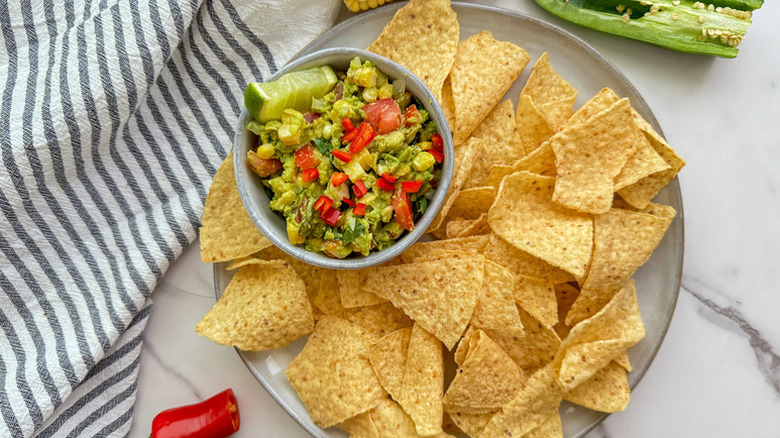 Bowl of corn and avocado guacamole on plate with tortilla chips