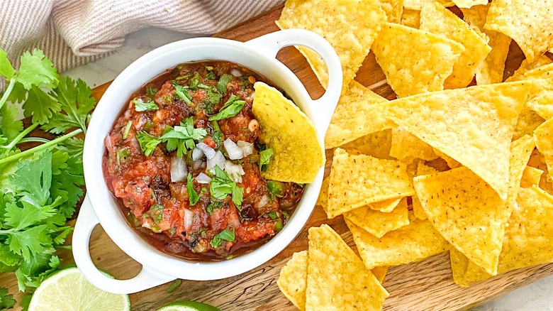 Bowl of fire-roasted tomato salsa next tortilla chips, with one chip dipped in the bowl