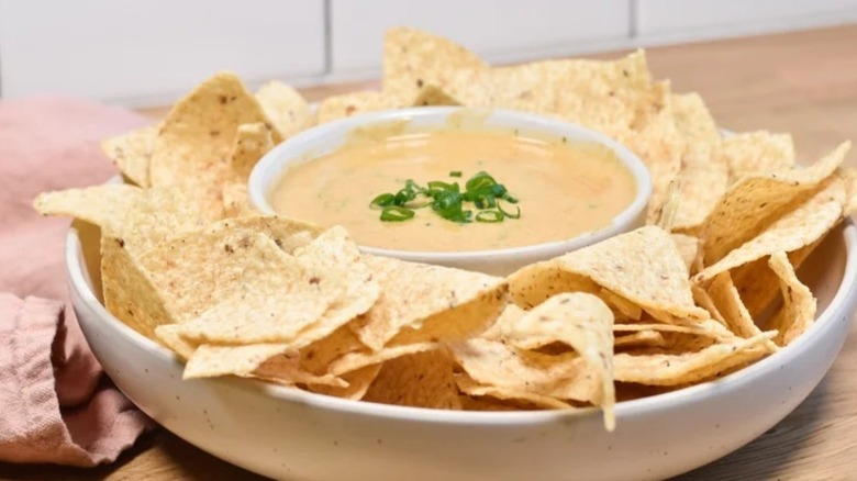 Bowl of white queso dip surrounded by tortilla chips