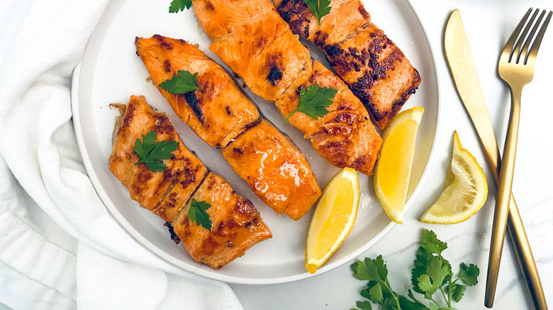 Four grilled salmon fillets on plate with parsley and lemon wedges