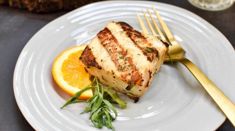 Grilled halibut on plate with orange slice and greens