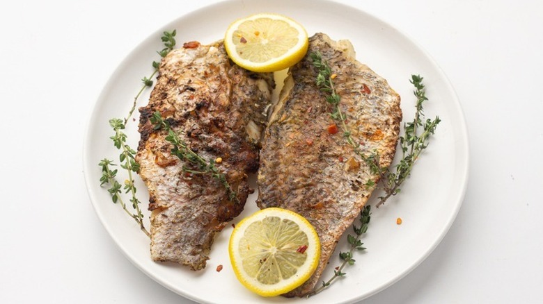Grilled barramundi on plate with thyme sprigs and lemon rounds
