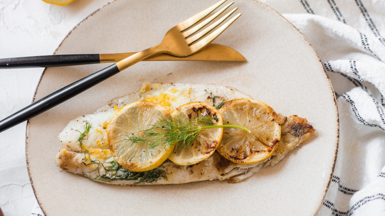 Grilled orange roughy on plate, topped with lemon rounds and dill