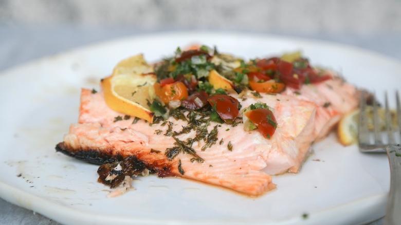 Grilled salmon on plate, topped with salsa and lemon slice