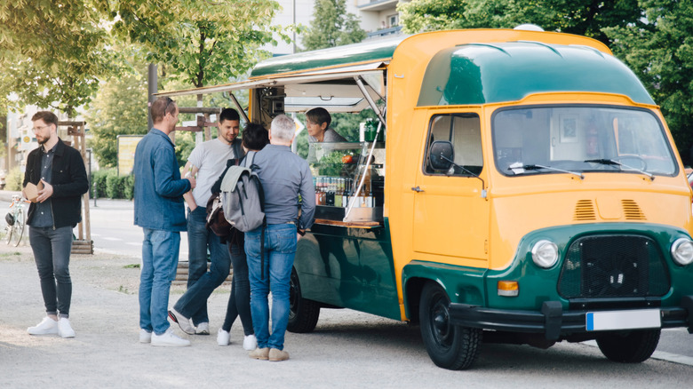 People standing at the window of a green and yellow food truck