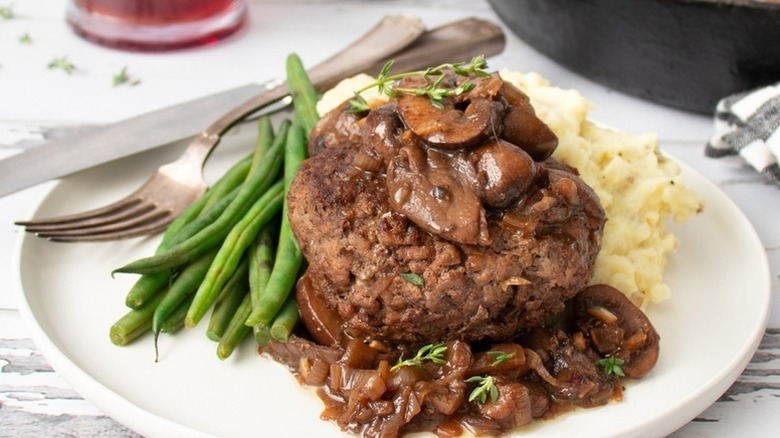 Plate of chopped steak topped with red wine mushroom sauce, served with green beans and mashed potatoes