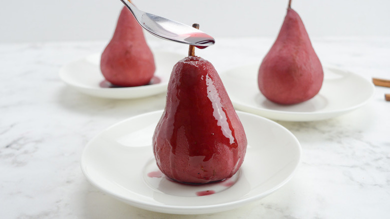 Spooning red wine sauce over poached pear on plate