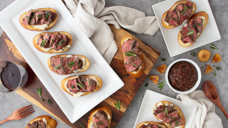 Steak-topped crostini on plates, next to bowl of fig jam