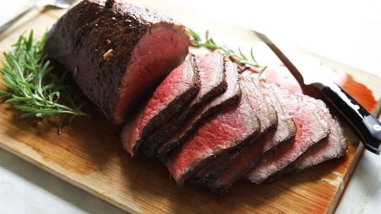 Sliced rump roast on wooden board with sprigs of rosemary