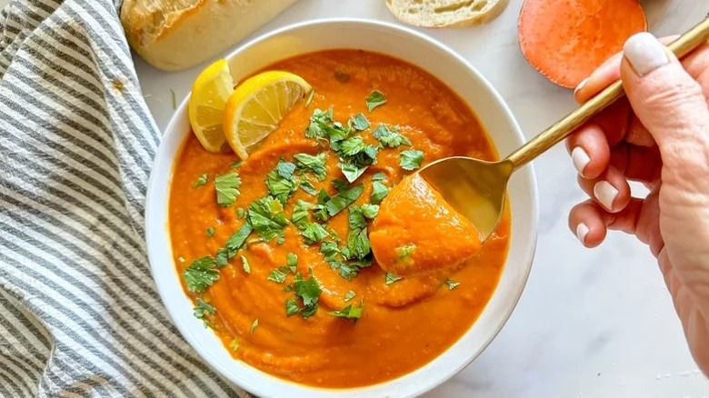 Hand lifting spoonful of sweet potato soup from bowl topped with lemon and cilantro