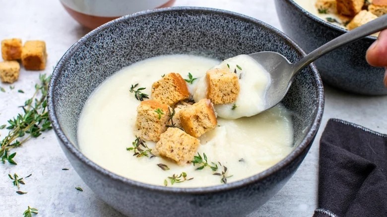 Spoon lifting cheesy cauliflower cheddar soup with thyme and crouton from bowl