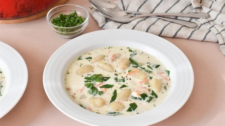 Gnocchi soup in bowl beside napkins, two spoons, and bowl of parsley