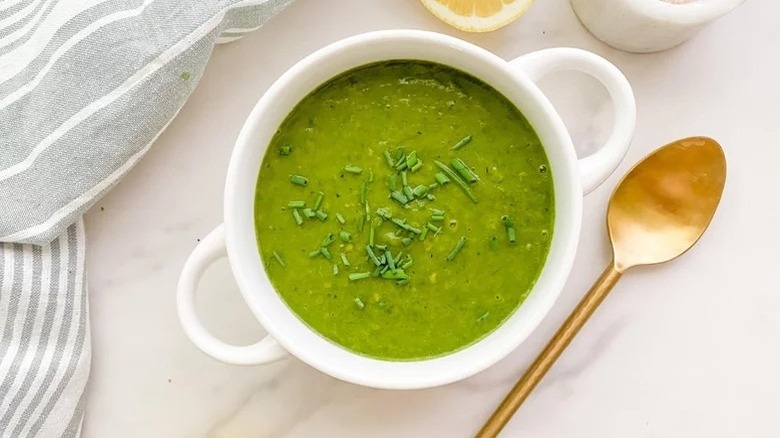 Bowl of spinach soup topped with chives, next to spoon