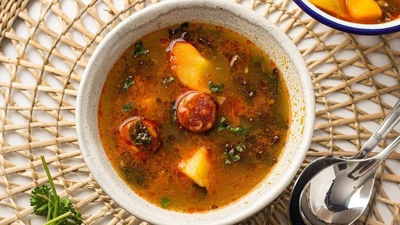 Two spoons and bowl of soup filled with chorizo, potatoes, and kale