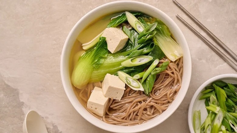Bowl of sesame noodles in broth, topped with tofu and bok choy