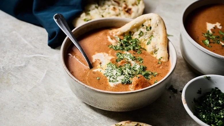 Chicken tikka masala soup in bowl with naan and spoon