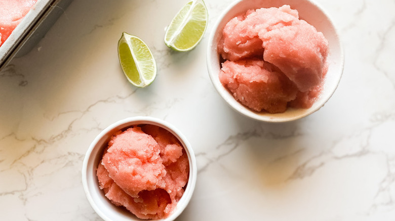 Watermelon sorbet in two white bowls, with lime wedges on the side