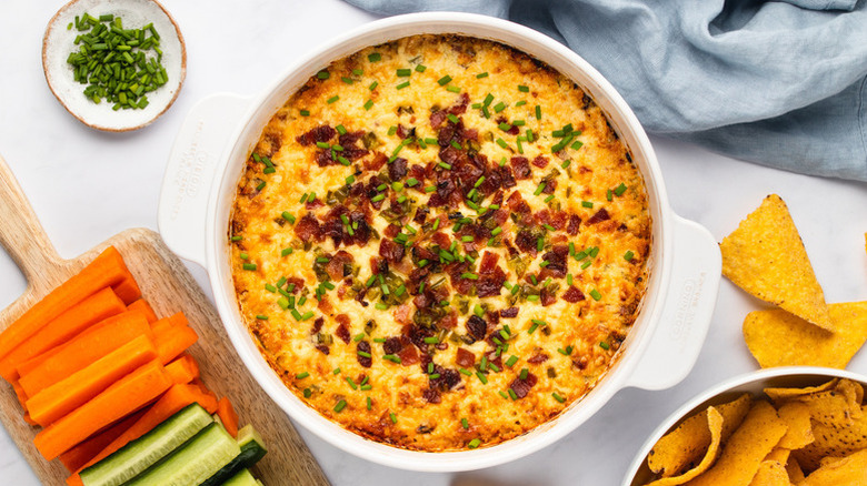 Cheesy dip in white casserole dish, topped with chopped bacon and chives