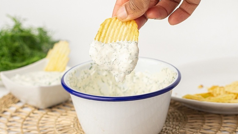 Dipping potato chip into bowl of creamy dill onion dip