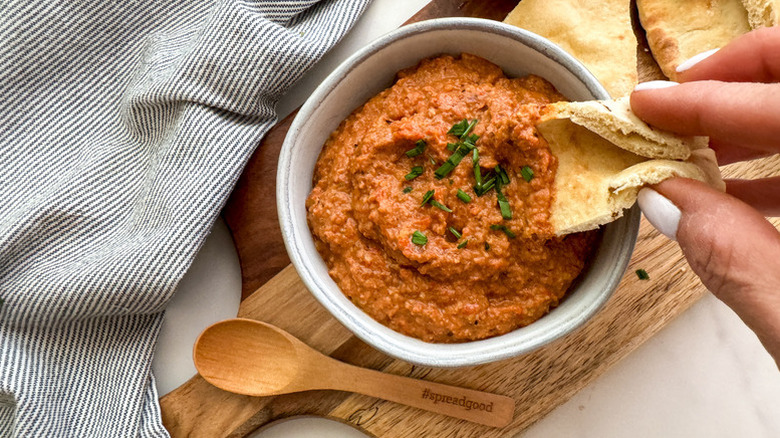 Dipping pita bread into bowl of red pepper dip