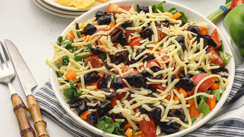 Bowl of taco dip with tomatoes, black olives, and shredded cheese
