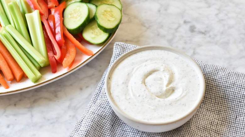Ranch dip in white bowl next to platter of crudites