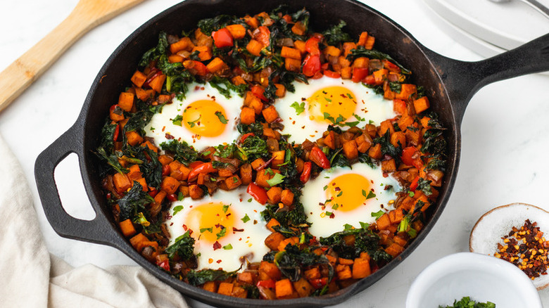 Kale and sweet potato hash in skillet with eggs baked in