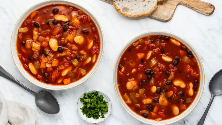 Two bowls of smoky bean and vegetable soup with fresh parsley on the side