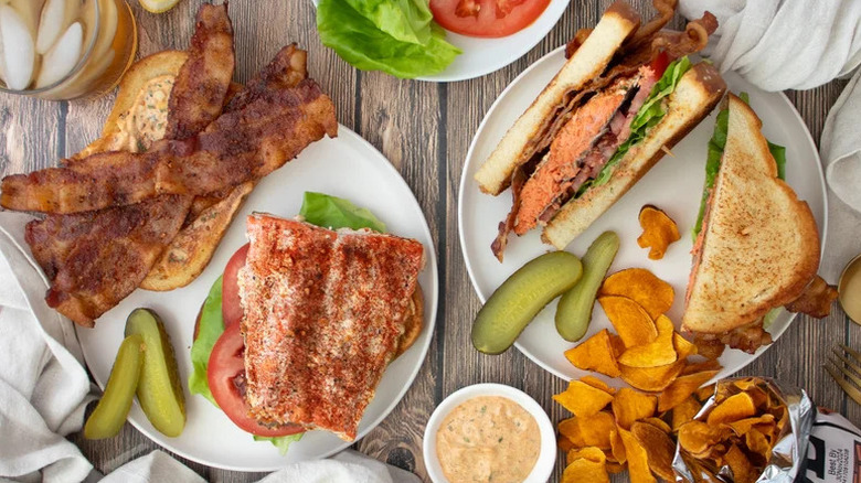Ultimate Louisiana Salmon BLTs on white plates with pickles and chips