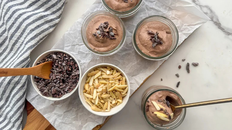Glass jars of Keto Chocolate Mousse on white parchment paper
