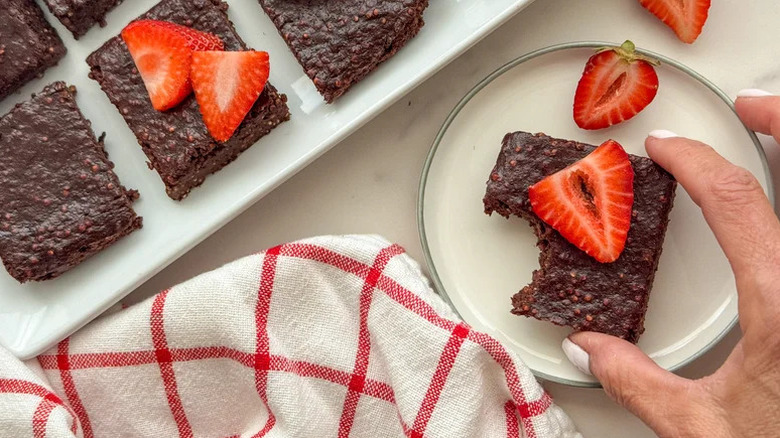 Hand reaching for Quinoa Cacao Brownie on white plate