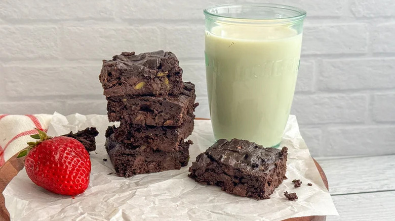 Vegan Avocado Brownies stacked on white parchment paper with glass of milk
