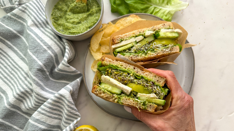 Hand holding half of green goddess sandwich on plate
