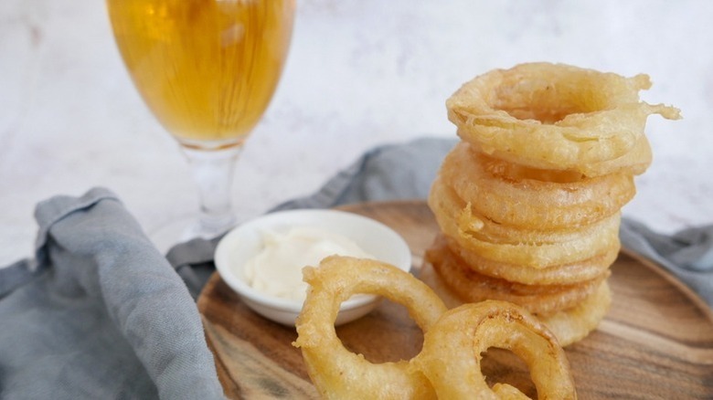 Stack of onion rings on wooden plate with bowl of creamy dip