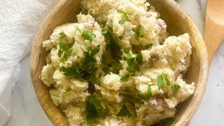 Herb-topped garlic mashed red potatoes in wooden bowl