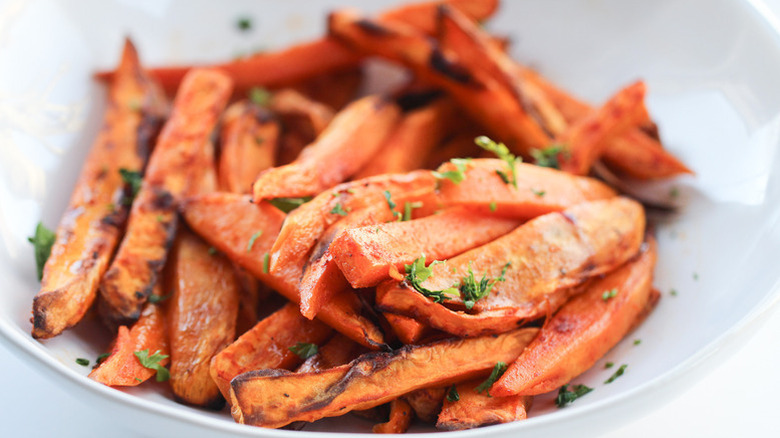 Sweet potato fries in bowl, topped with chopped herbs
