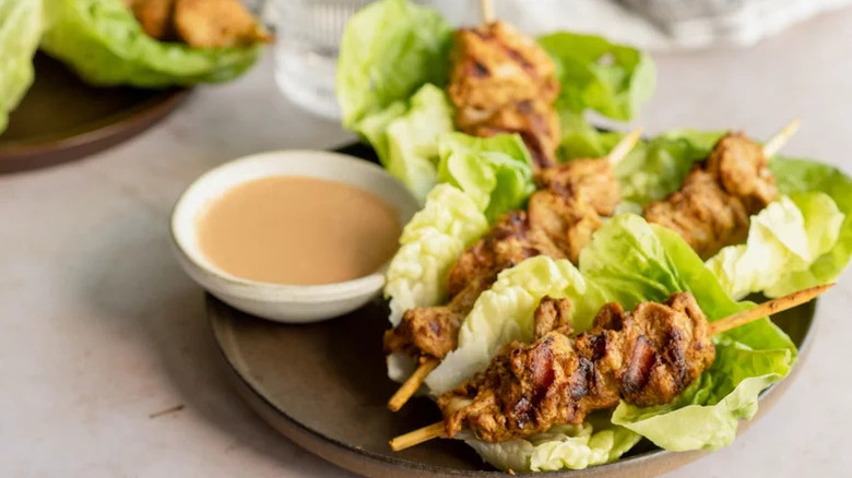 Satay-Style Chicken Lettuce Wraps on brown plate with bowl of sauce