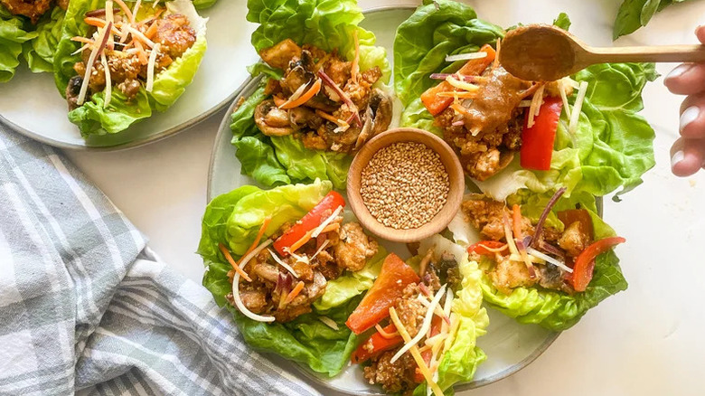 Spoon drizzling sauce on Thai Crispy Tofu Lettuce Wraps on white plate