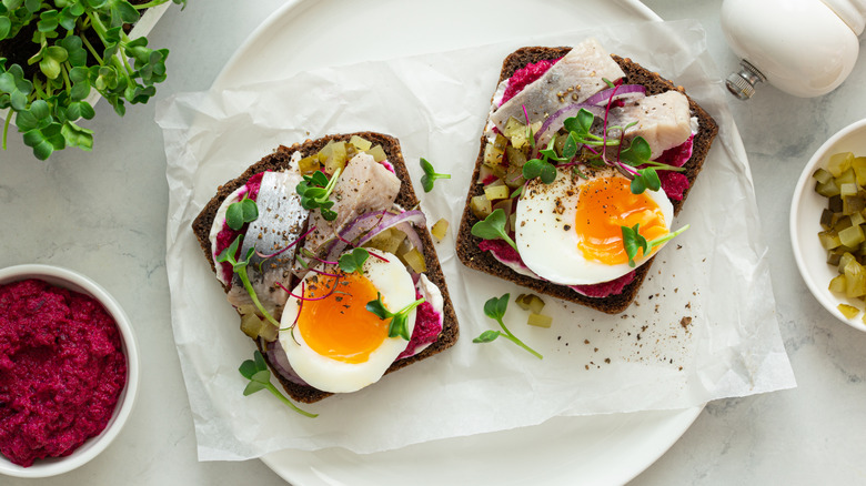 Smørrebrød two pieces of rye with fish, egg halves, and greens on marble table