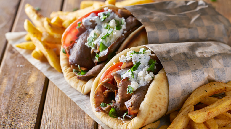 Two gyro wrapped in paper with fries