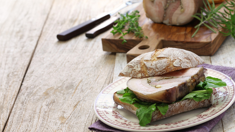 Porchetta sandwich on plate with pork in the background on cutting board