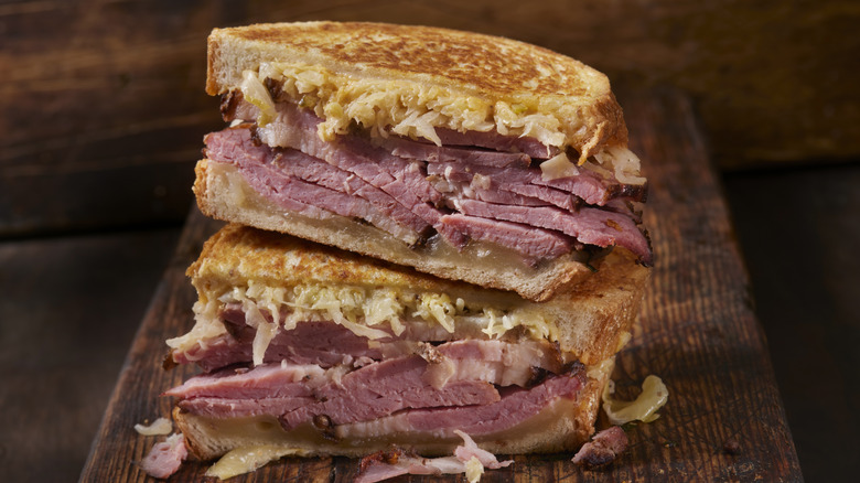 Two halves of a pastrami sandwich stacked on top of each other wood background