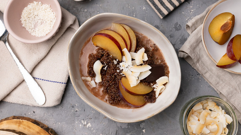 Quinoa breakfast bowl with sliced plums, shredded coconut, and dark chocolate