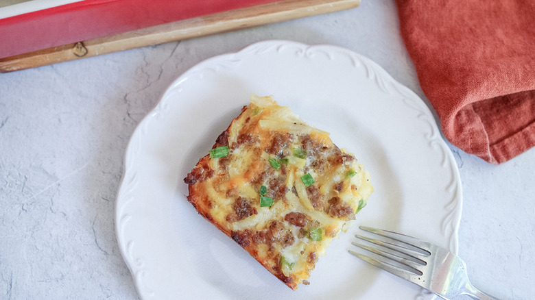 Slice of cheesy breakfast casserole on white plate with fork